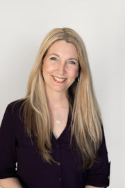 A woman with long blonde hair smiles, wearing a necklace and bracelet, representing WeNatal's focus on wellness and positivity.